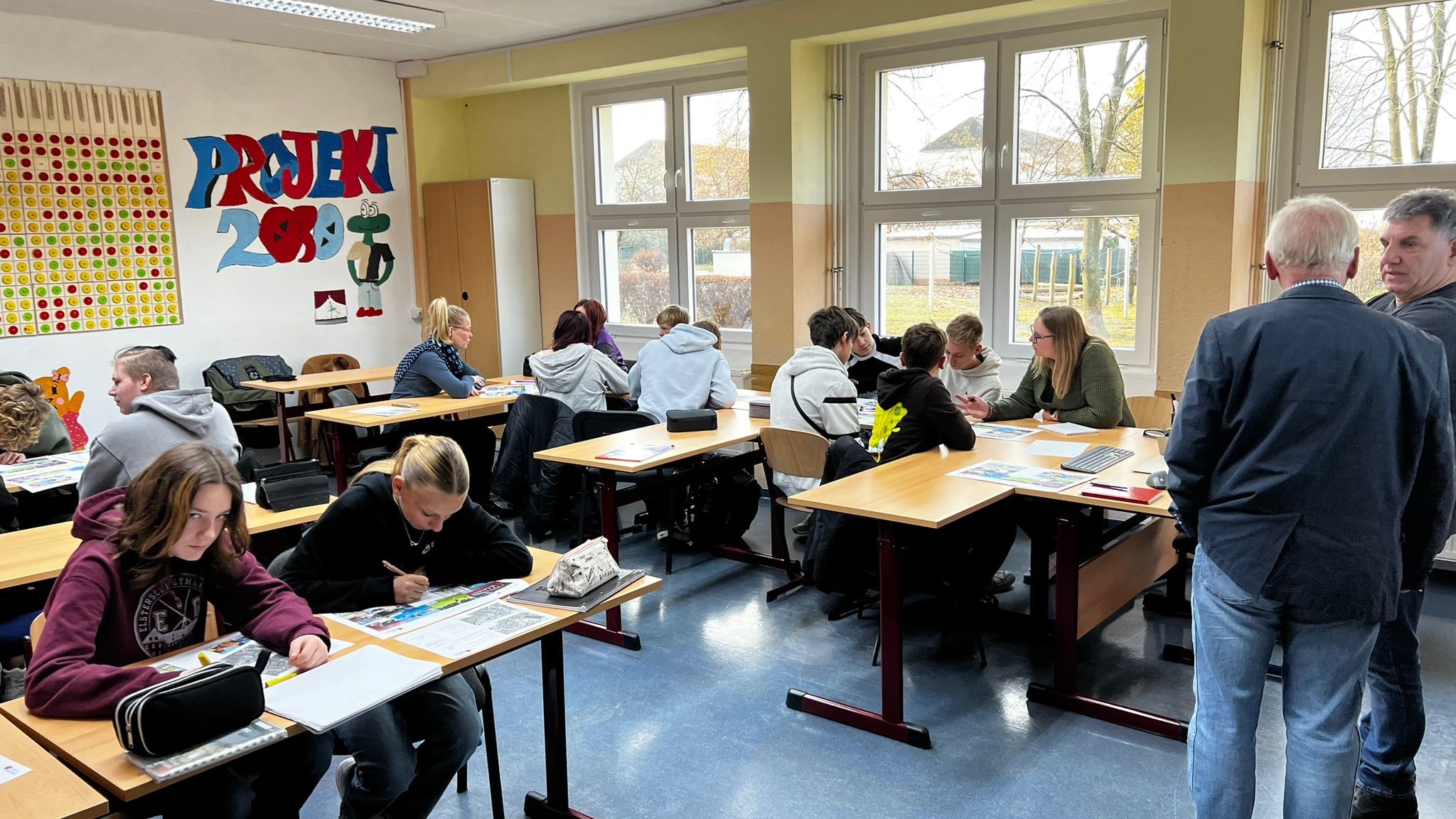 Schülerinnen und Schüler sitzen in Arbeitsgruppen zusammen in einem Klassenraum.  