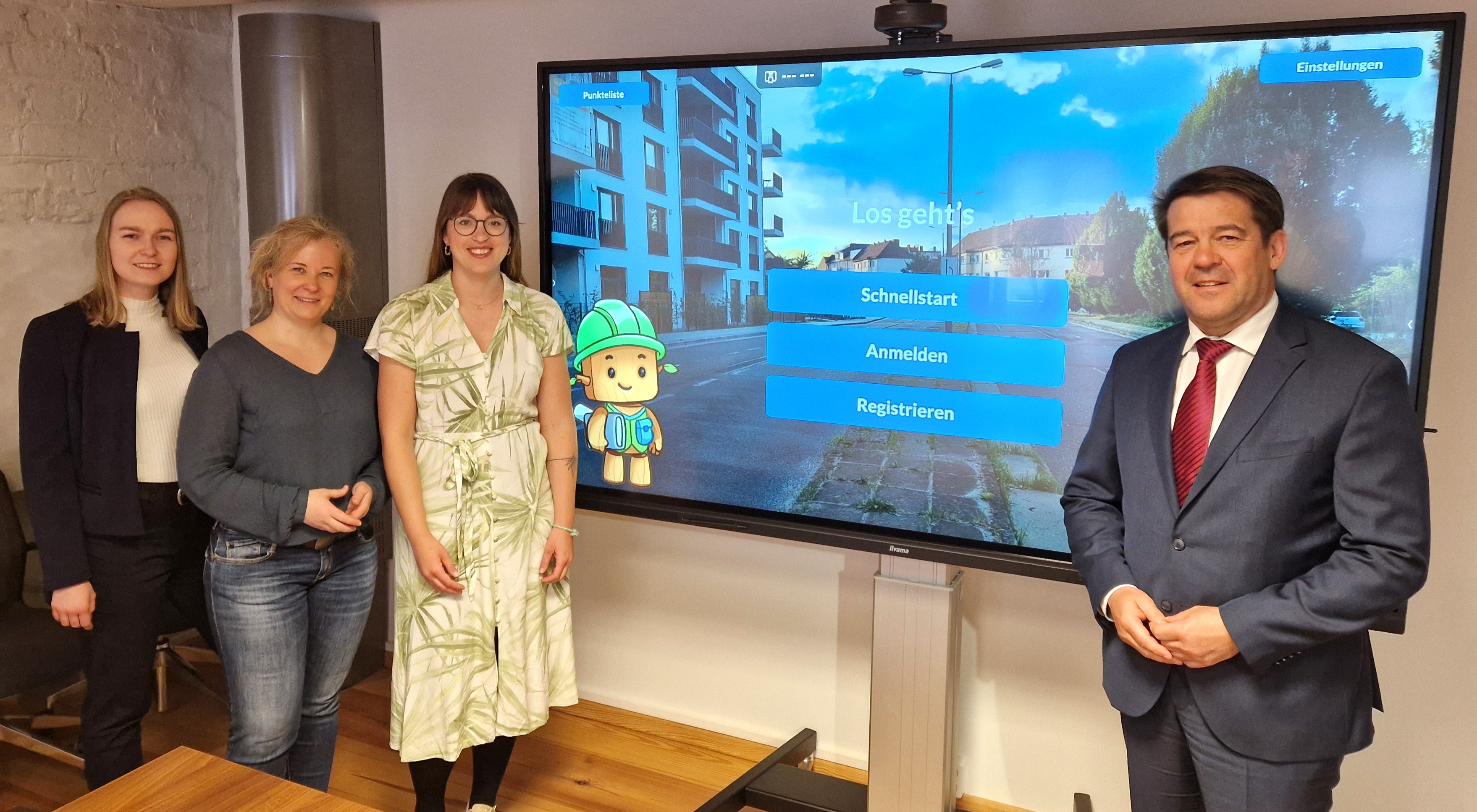 Drei Mitarbeiterinnen des Projekts und der Oberbürgermeister stehen vor einer interaktiven Tafel mit der Startansicht des Planspiels in Brandenburg an der Havel.  