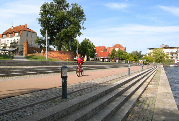 Blick auf das Bollwerk am Wasser und ein vorbeifahrendes Kind auf einem Fahrrad
