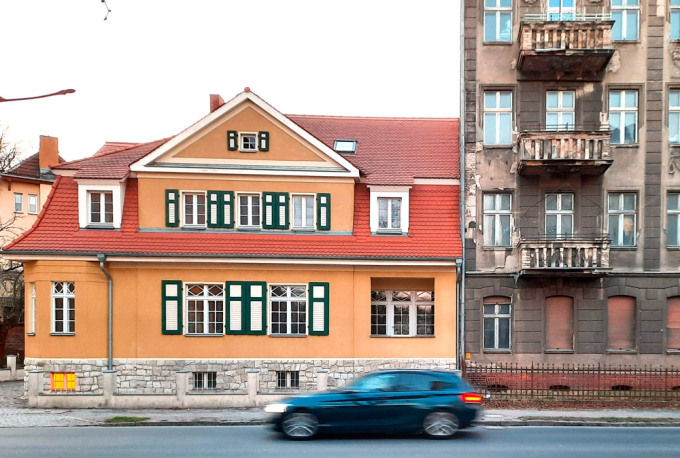 Zwei Gebäude an einer Straße in Zossen mit vorbeifahrendem Auto